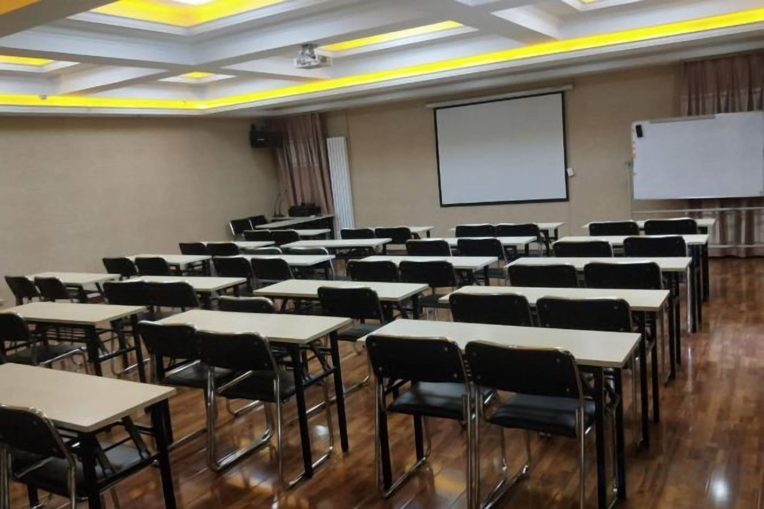 A conference room with rows of tables and chairs, a projector screen, and a whiteboard.