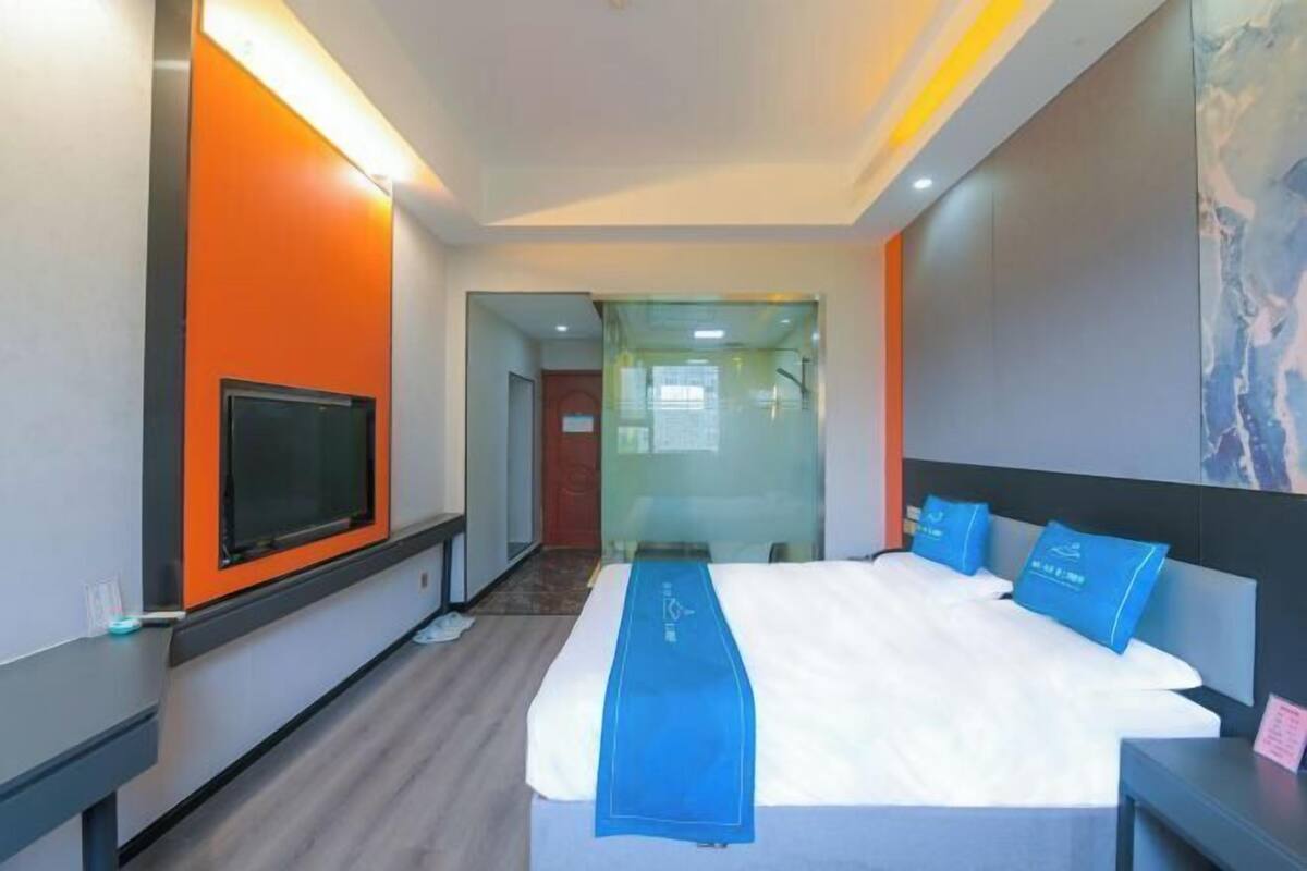 Habitación de hotel con cama, televisor, separador de vidrio y corredor azul para la cama.