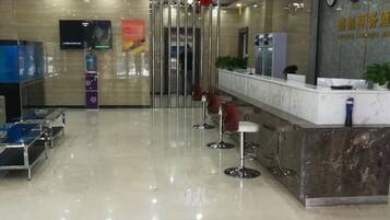 A hotel reception area with a marble counter, a television, and a seating area with bar stools.