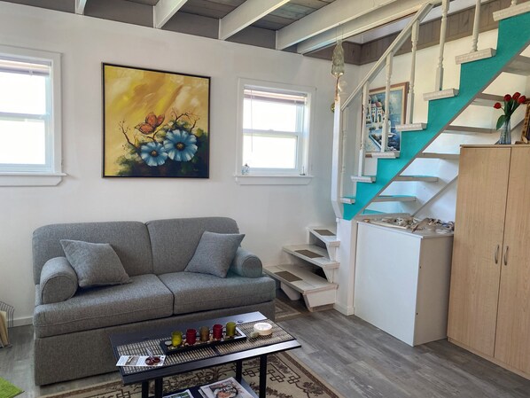 Ein Wohnzimmer mit grauem Sofa, einem Blumenbild, einer Treppe und einem Holzschrank.