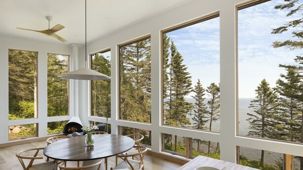 Una habitación amplia con ventanas grandes que ofrecen vistas a un bosque y una masa de agua.