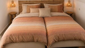 Un dormitorio con techo inclinado, cabecera de madera, dos mesitas de noche y una cama con ropa de cama a rayas.