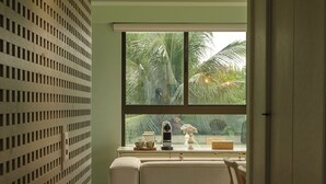 Ein schmaler Flur mit Wandverkleidung, einem Fenster mit Blick auf Palmen und einer kleinen Sitzecke mit Tisch und Stühlen.