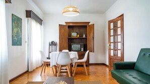 Un comedor con una mesa y sillas, un televisor sobre una estantería de madera y un sofá verde.