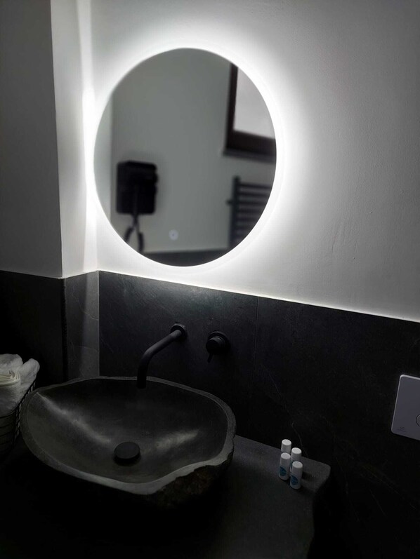 Un bagno moderno con uno specchio rotondo, lavabo scuro e design minimalista.