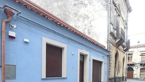 A narrow street with a blue building featuring a small entrance and a window with shutters.