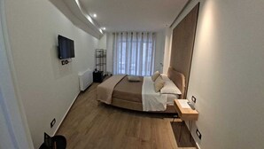 A modern hotel room with a bed, a bedside table, a TV mounted on the wall, and a window with curtains.