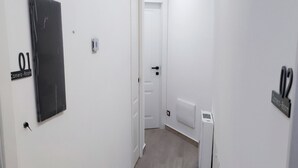 A narrow hallway with white walls and wooden flooring, leading to a door labeled "Camera-Room".