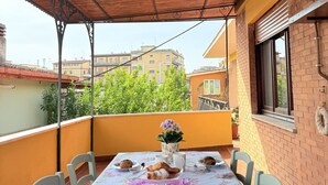 Eine überdachte Terrasse im Freien mit einem für eine Mahlzeit gedeckten Tisch, mit einer blumigen Tischdecke und einer Blumenvase.