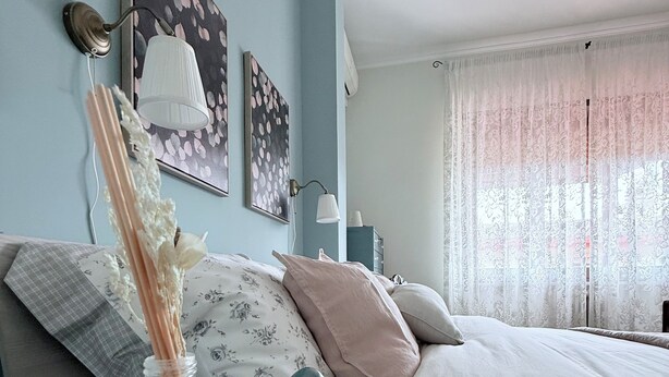 Ein Schlafzimmer mit einem Bett, einem Nachttisch mit einer Vase und Wandbildern.