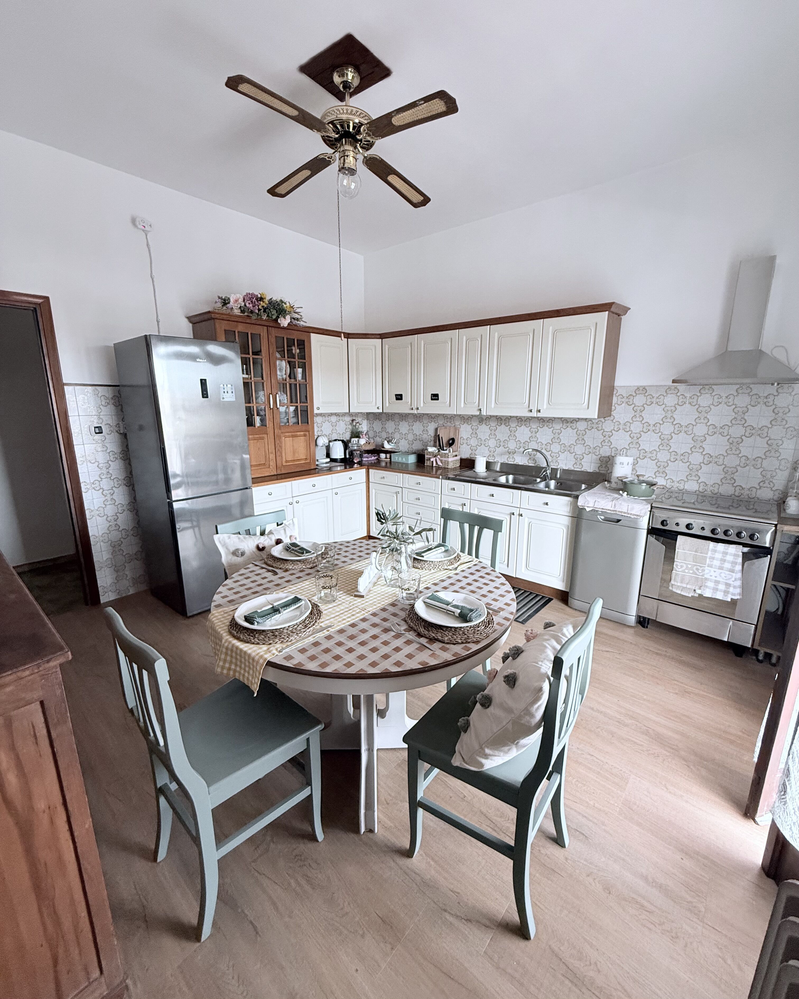 A kitchen with white cabinets, a stainless steel refrigerator, a stove, and a dining table set for four.
