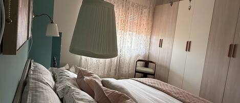Un dormitorio con dos camas, una mesita de noche, una lámpara, una silla y un armario.