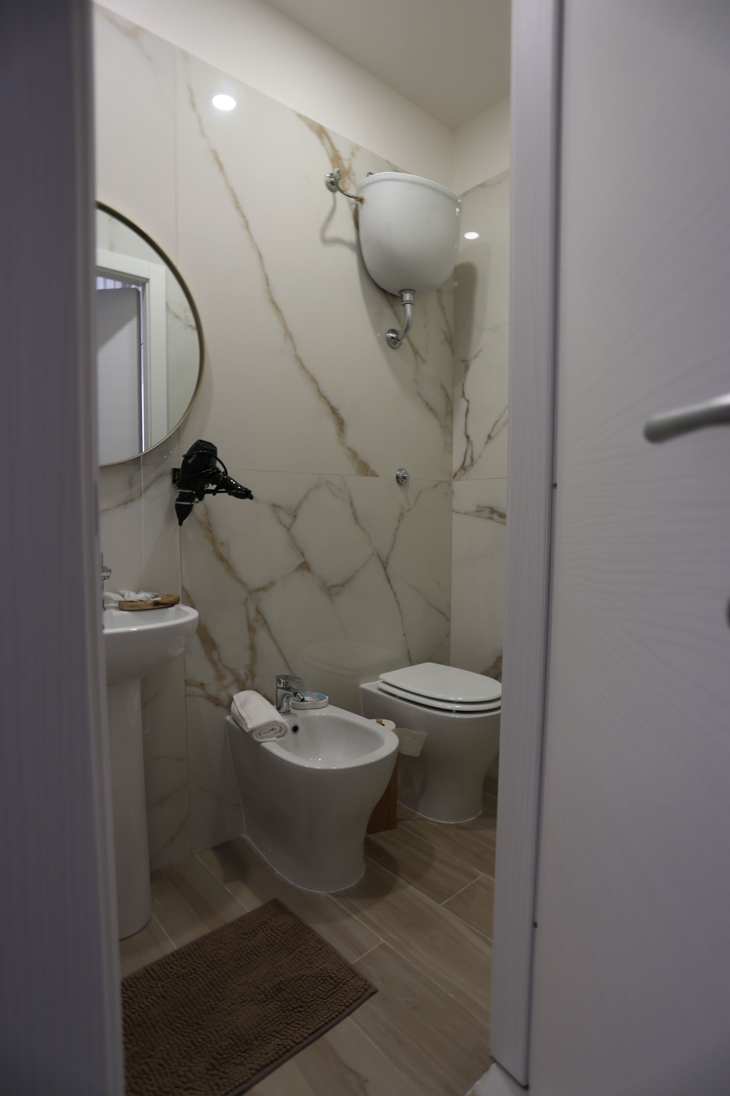 Une salle de bain avec un mur en marbre, un lavabo, un bidet et des toilettes.