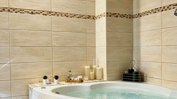 Une salle de bain avec une baignoire sur pieds, un tabouret en bois et des articles de toilette rangés sur une étagère.