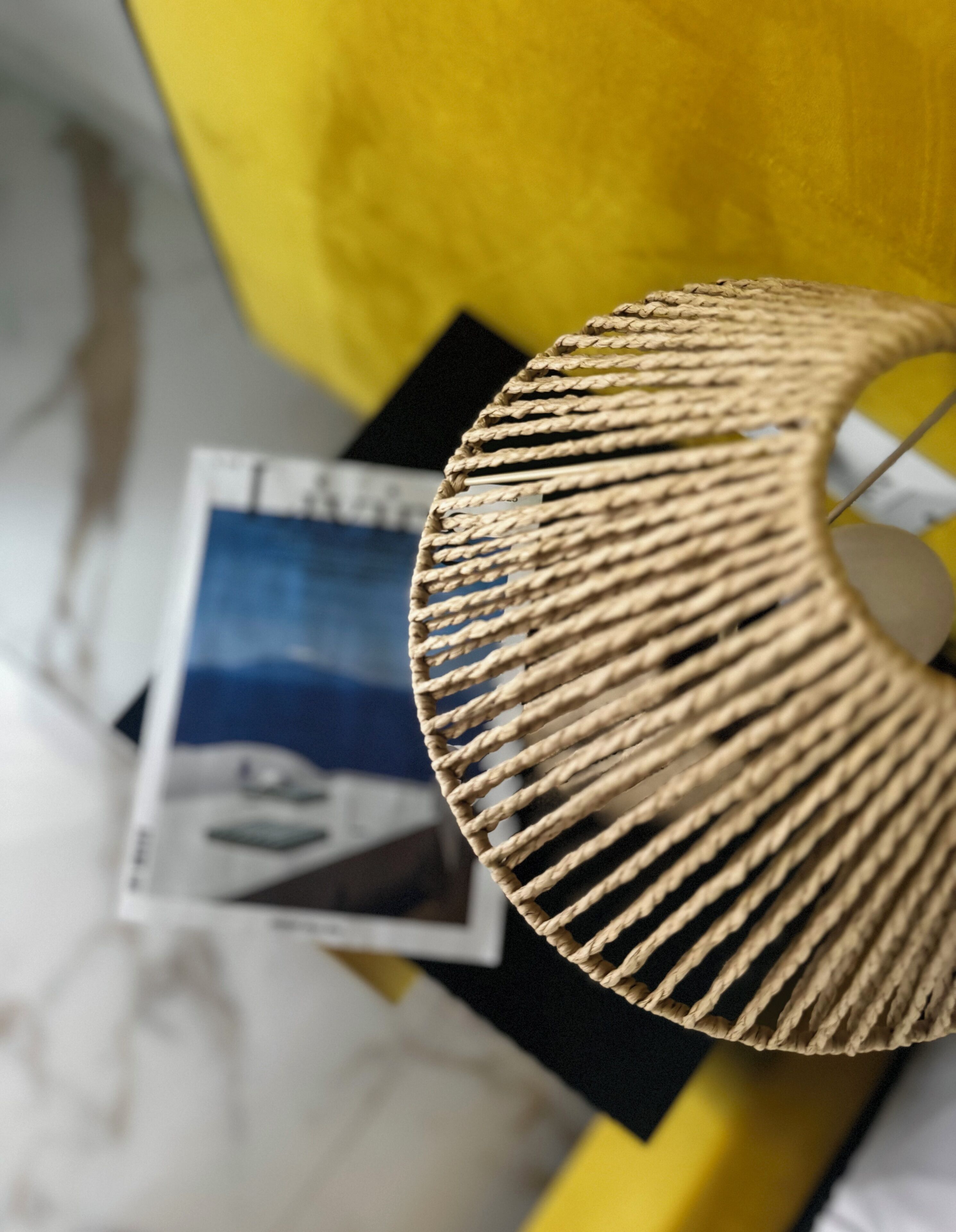 Un primo piano di una lampada intrecciata con un motivo circolare, posata su una superficie con sfondo giallo e una rivista o brochure.