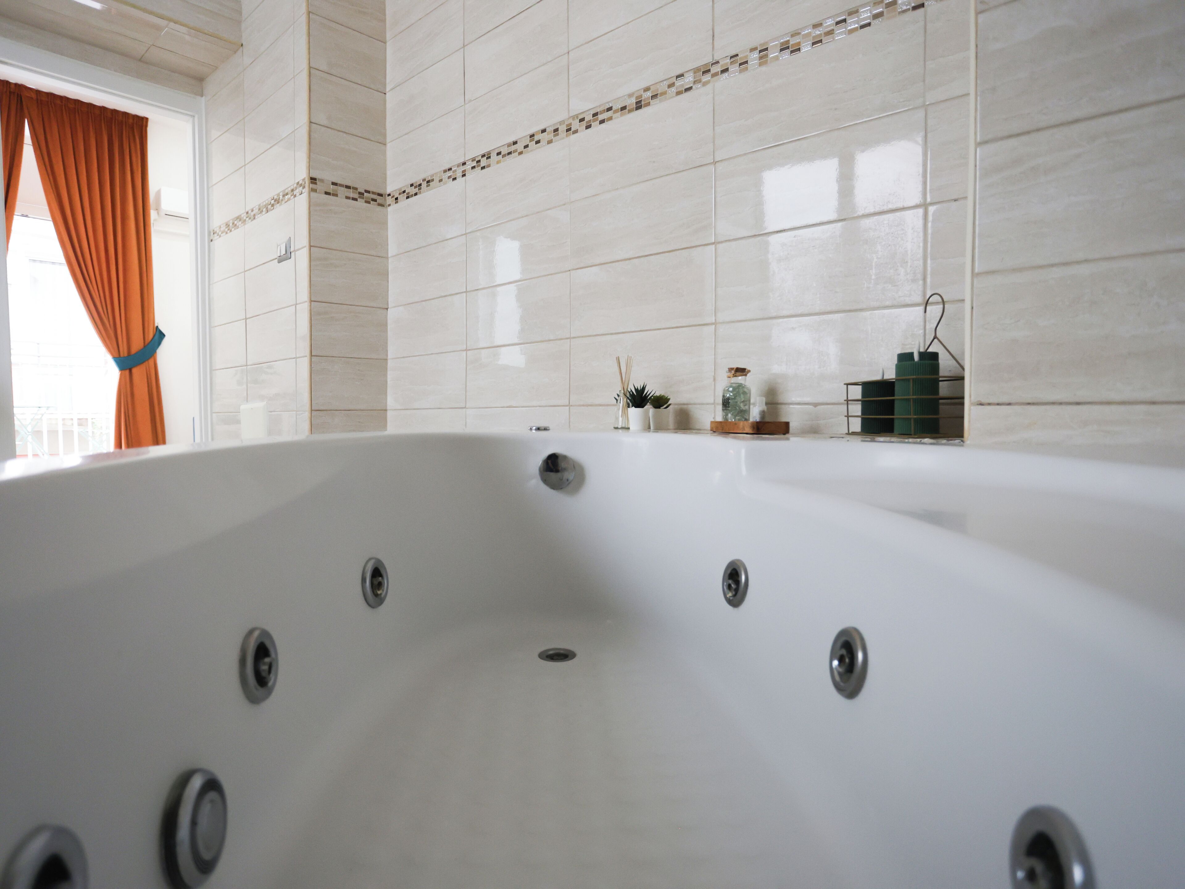 Ein modernes Badezimmer mit einer großen Badewanne, gefliesten Wänden und einem Fenster mit Vorhängen.
