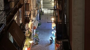 Une rue étroite bordée d’immeubles à plusieurs étages dotés de balcons, de lampadaires et d’un scooter garé sur le trottoir.