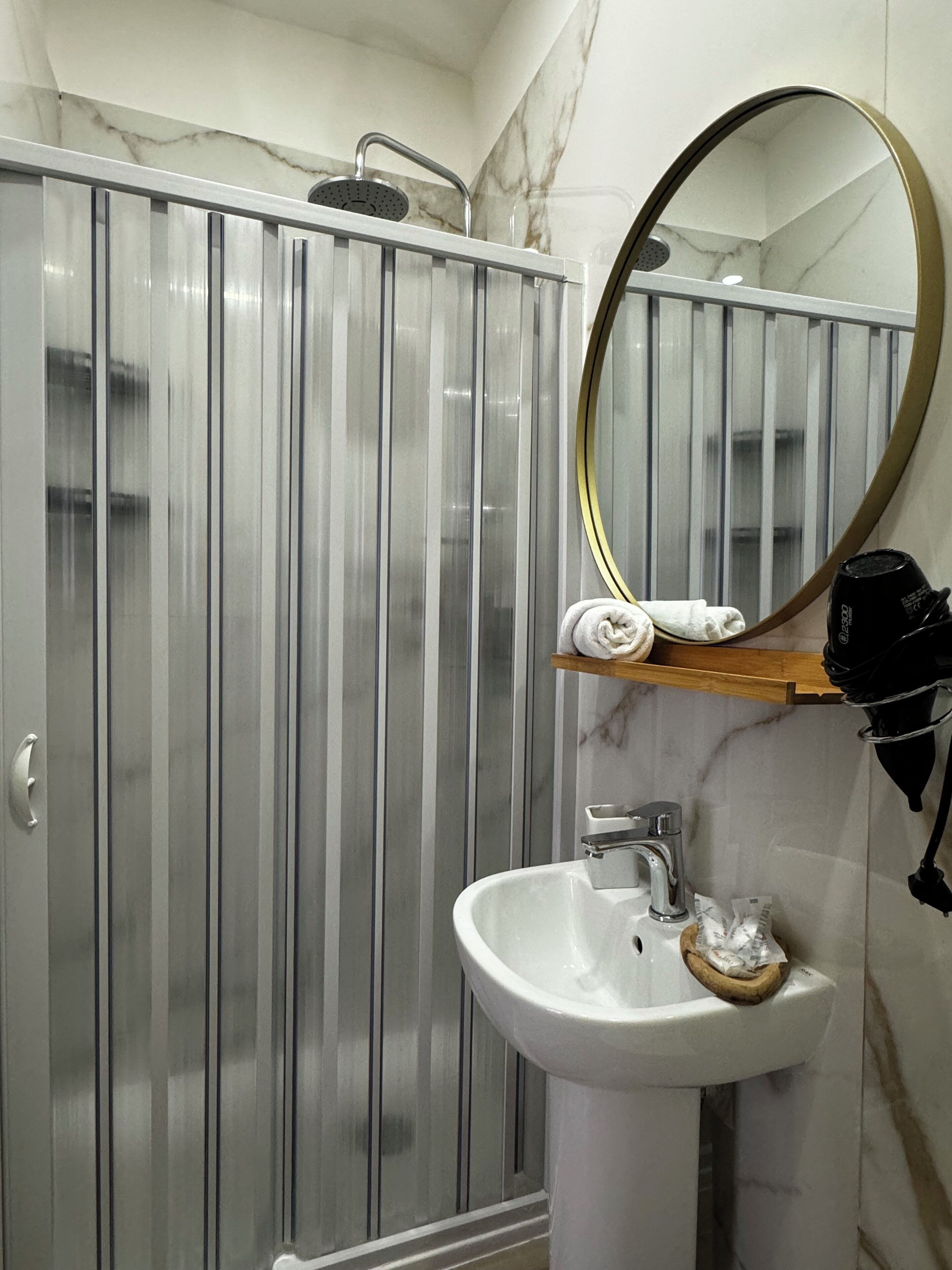 A bathroom with a marble vanity, a sink, a mirror, and a shower enclosure.