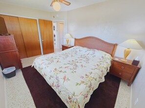 Ein Schlafzimmer mit einem Bett, einem Holzschrank, Nachttischen mit Lampen und einem Deckenventilator.