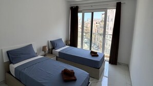 Una camera da letto con due letti, una finestra con tende, una lampada a soffitto e vista sugli edifici.
