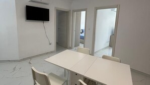 Una camera moderna con un tavolo e sedie bianche, una TV a schermo piatto montata a parete e un condizionatore d'aria.