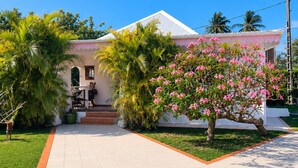 A house with a tiled driveway, a porch with chairs, and a garden with palm trees and flowering plants. - Villa Sainte-Anne (Sainte-Anne)
