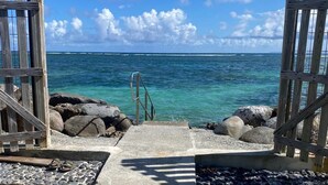 A wooden gate leading to a beach with clear turquoise water and a rocky shoreline. - Villa Sainte-Anne (Sainte-Anne)