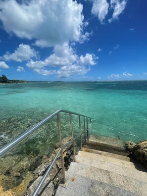 Vista despejada de una escalera que lleva a una playa con agua turquesa y una barandilla de metal.