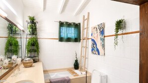 A bathroom with a bathtub, toilet, and sink, with plants and artwork on the walls. - Villa Sainte-Anne (Sainte-Anne)