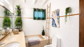 Un bagno con vasca, WC e lavabo, decorato con piante e opere d'arte alle pareti.