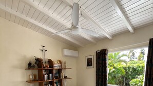 A room with two single beds, a bookshelf, a ceiling fan, an air conditioning unit, and a window with curtains. - Villa Sainte-Anne (Sainte-Anne)