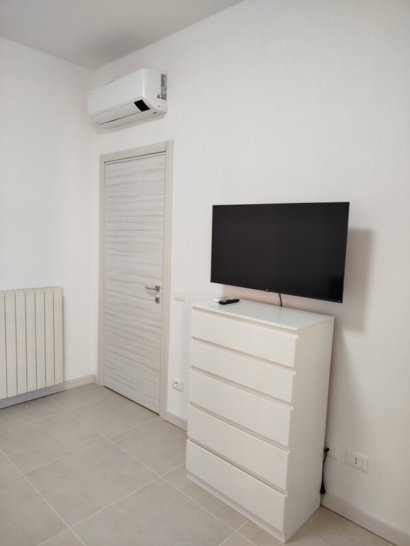 Een kamer met een witte radiator, een witte garderobe en een televisie op een witte dressoir.