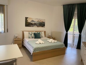 Een slaapkamer met een bed, nachtkastjes, een bureau en een raam met gordijnen.