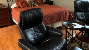 Een slaapkamer met een bed, een zwarte leren fauteuil, een tafeltje en een houten dressoir.