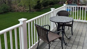 Een terras met een witte reling, twee rieten stoelen en een ronde tafel.