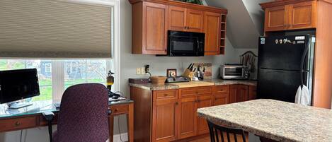 A kitchen with wooden cabinets, a microwave, a toaster, a refrigerator, and a dining area with a chair.
