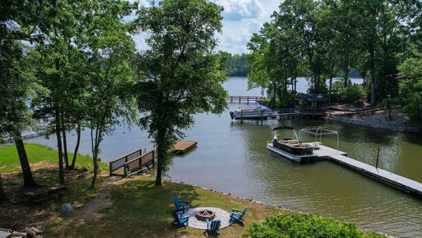 Une vue sur le lac, avec un quai, un bateau et un espace pique-nique équipé de chaises et d’un foyer.