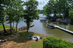 A lakeside view with a dock, a boat, and a picnic area with chairs and a fire pit.