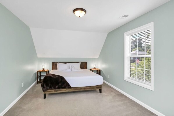 A bedroom with a bed, nightstands, a window with blinds, and a ceiling light.