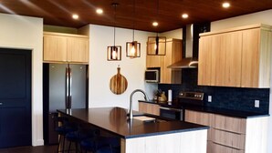 Une cuisine moderne dotée d’un îlot central, de tabourets de bar, de meubles en bois, d’appareils électroménagers en acier inoxydable et de luminaires suspendus.