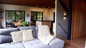 Un salon moderne avec un canapé gris, un escalier en bois et une cuisine en arrière-plan.