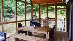 Une terrasse en bois avec une table et des chaises, un fauteuil suspendu et un espace barbecue.