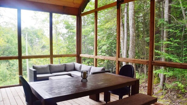 Une terrasse en bois avec une table et des chaises, un canapé et une grande fenêtre donnant sur une forêt.
