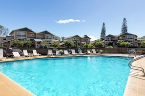 A swimming pool with lounge chairs and a building complex in the background.