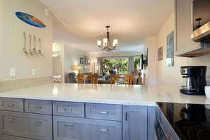 A kitchen with a central island, cabinets, a coffee maker, and a dining area with chairs and a table.