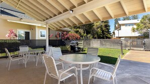 A covered patio area with a round table and chairs, a grill, and a view of the surrounding neighborhood.