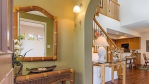 A spacious living area with a high ceiling, a staircase, and a dining area with wooden furniture. - Pools, Gym & BBQ, Near Beach & Golf, Tennis (Waikoloa Village)