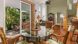 A spacious living room with a glass dining table surrounded by chairs, a ceiling fan, and a view of greenery outside. - Pools, Gym & BBQ, Near Beach & Golf, Tennis (Waikoloa Village)