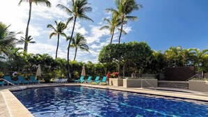 Une piscine à l’eau d’un bleu cristallin, entourée de chaises longues et de palmiers.