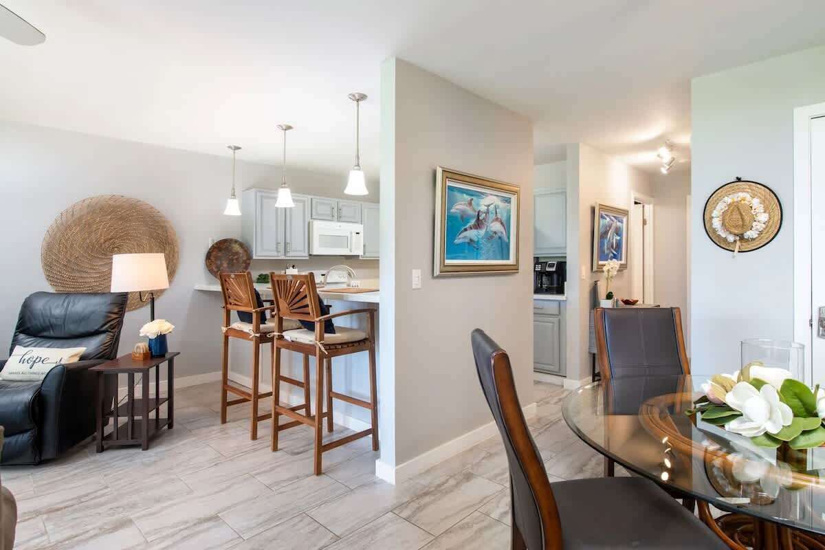 Open concept with pendant lights, bar stools, and a view from kitchen to dining and entry hallway.

